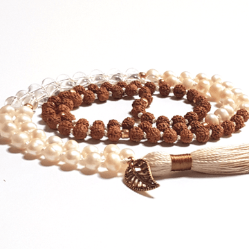 Close up of chndmade Pearl, Quartz and Rudraksha Mala necklace with leaf charm on tassel curled on the table